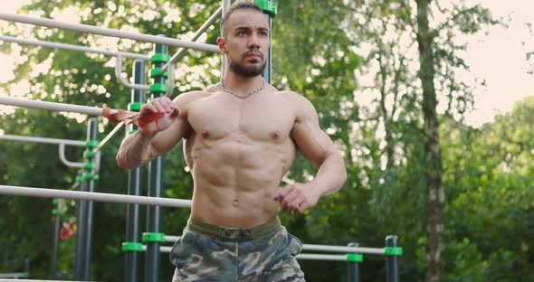 Handsome Shirtless Sportsman Building Muscles Training with Resistance Band in Nature