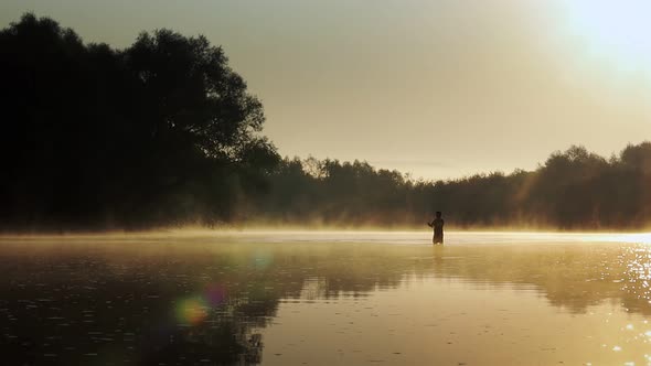 Silhouette of a fisherman on the river on a foggy summer morning.