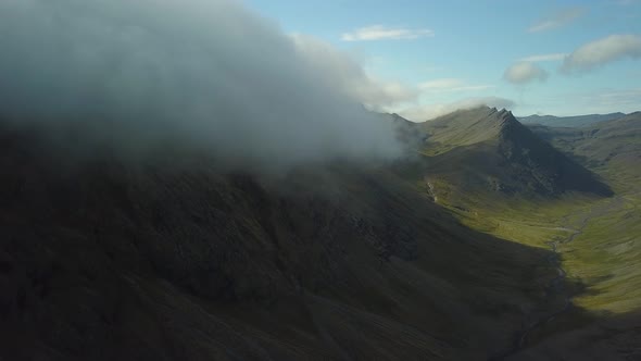 Aerial of green valley and stream of water between verdant hills covered in clouds in Djúpivogur sma