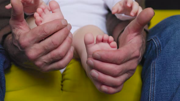 Close Up Grandpa Hands Holding Baby's Feet Playing with Newborn