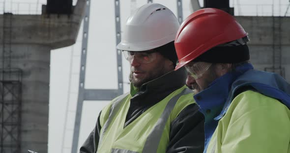 Male Engineers Discussing Bridge Drafts on Tablet