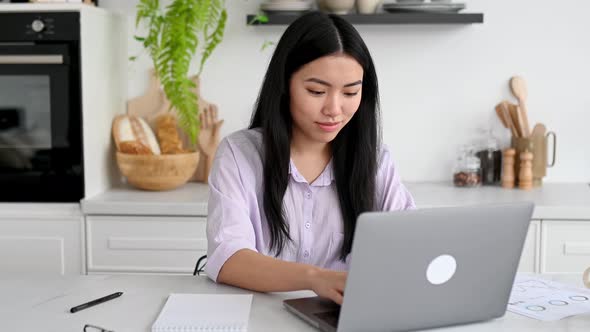 Smart Lovely Positive Asian Brunette Girl in a Shirt Designer Freelancer or Student Sits at Home in