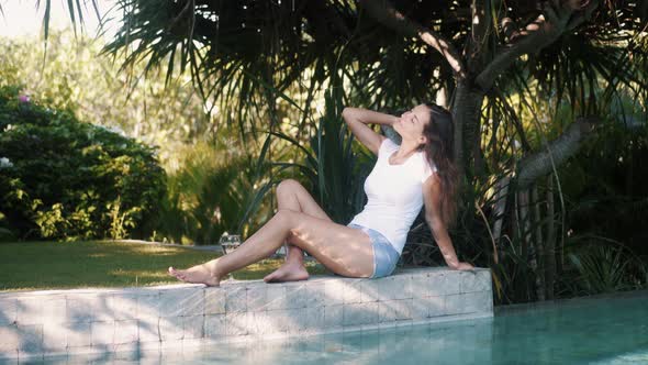 Woman in Casual Summer Clothes Sits on Edge of Pool Rests and Enjoys Vacation