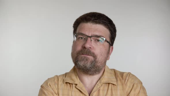 Man with a beard and glasses looks and talks thoughtfully on a gray background.