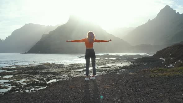 A Woman Walks Next to the Ocean and Raises Her Hands Up and Enjoying the Moment on Volcanic Beach of