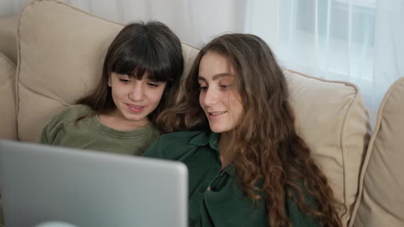 Couple of Beautiful Cheerful Young Women Smiling While Watching Film on Computer on Sofa