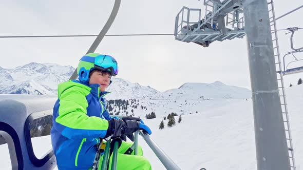 Cute Boy with Ski Going Up on Chairlift in Mountains