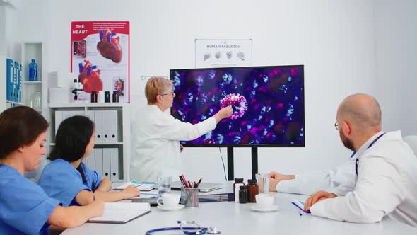 Elderly Medic Presenting Virus Evolution Pointing on Display in Hospital Office