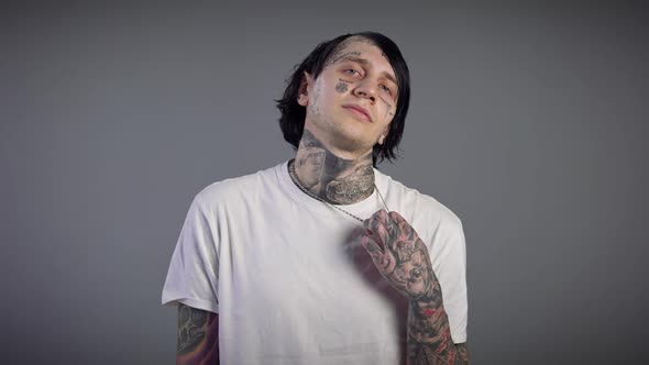 Front View of Confident Young Tattooed Man Stretching Neck and Hands Exercising at Grey Background