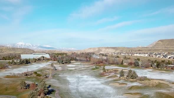 Winter aerial shot of a golf course with wind turbines in the distance - PARALLAX - zooming out duri