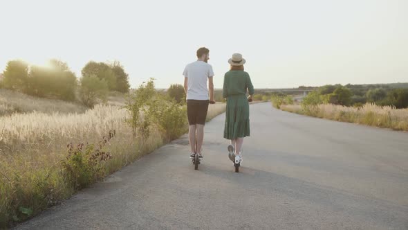 Beautiful Couple in Love Riding Together on Electric Scooters on Asphalt Road