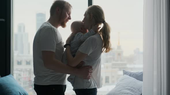 young family with baby hugging while standing by the window