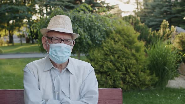 Portrait of Senior in Medical Mask Looking Into Camera While Sitting on Bench