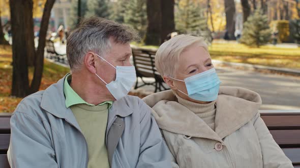 Elderly Family Couple in Medical Masks Sit in Autumn Park Mature Man Turns Away Resentfully Crossing