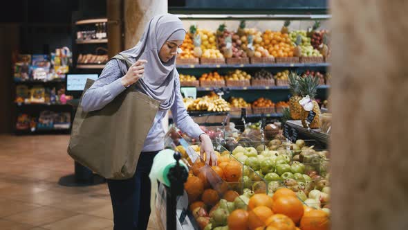 Portrait of Young Muslim Woman in Hijab Choosing Fruits in the Supermarket