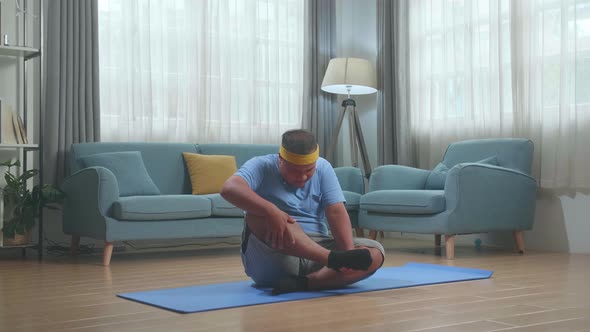 Fat Asian Man On Mat Trying Doing Yoga In Gomukhasana Pose At Home