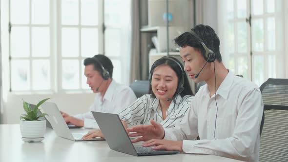 A Woman Of Three Asian Call Centre Agents Wearing Headset And Helping A Man To Work With Computer