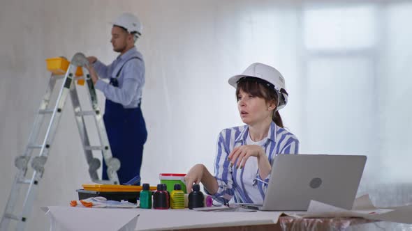 Woman in Safety Helmet Due To Trouble New Interior Design at Construction Site Sitting at Laptop and