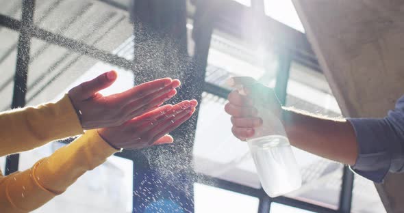 Mixed race male cafe worker wearing face mask disinfecting hands of female coworker