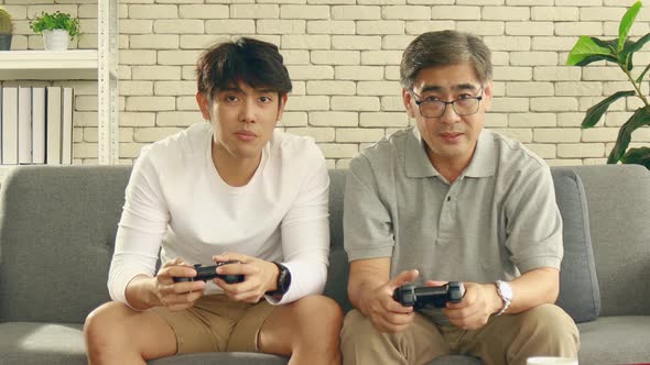 Asian father and son happily enjoy video games at home on vacation