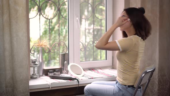 Young Woman in Front of the Window Combing Her Hair. Hair Care.