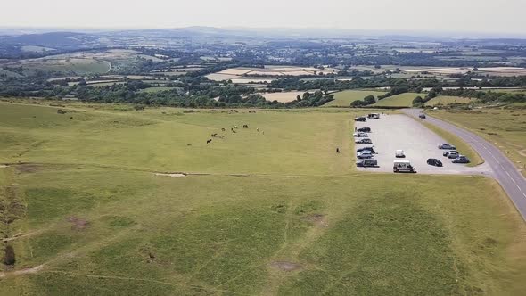 Drone footage; Travel in of a parkinglot alongside a highway in Devon, UK. Green Scenery and cars.