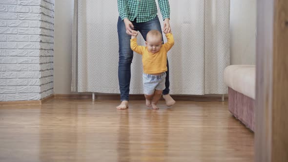Mom teaches the child to walk holding his hands