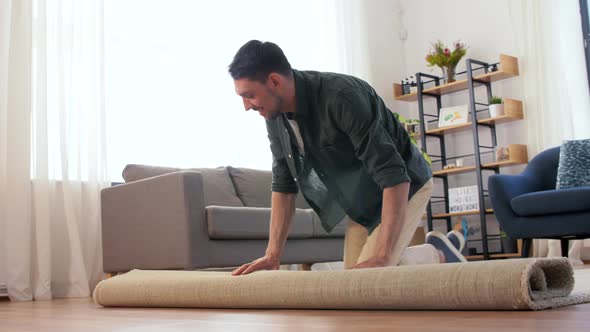 Happy Smiling Young Man Unfolding Carpet at Home