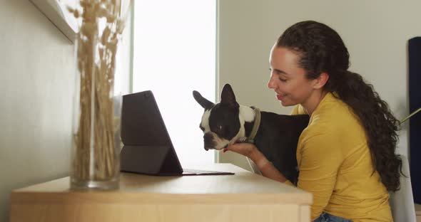 Happy caucasian woman kissing her dog and using tablet