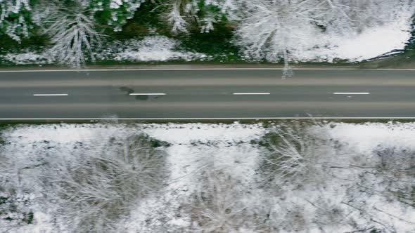 Empty street in a snow covered forest, flying straight from right to left by drone in a top down vie