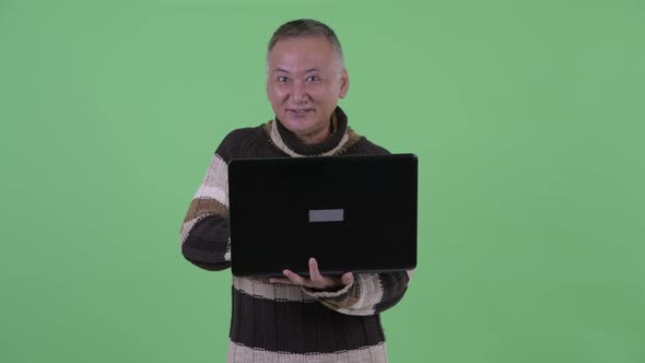 Happy Mature Japanese Man Thinking While Using Laptop and Talking
