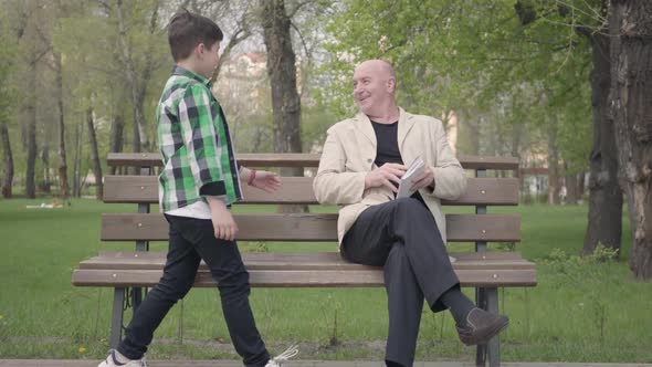 The Bald Mature Man Sitting in the Park on the Bench Reading a Book