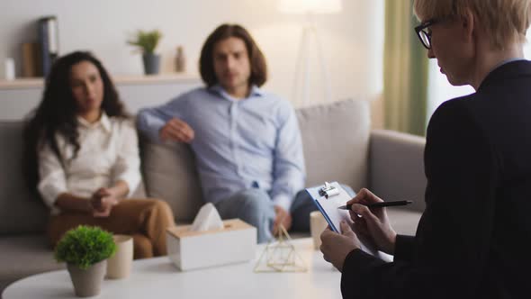 Female Psychotherapist Taking Notes Writing Diagnosis of Young Spouses with Relationship Problems