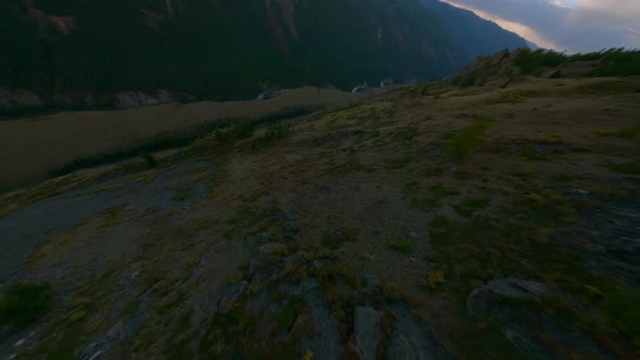 FPV Sport Drone Speed Dive Mountain Peak Over Stone Dry Grass Hilly Terrain and River at Evening