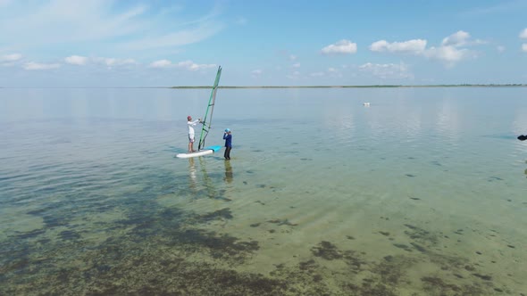 Aerial Drone Footage of Windsurf Instructor Teaching Woman Beginner To Standing on Surfboard