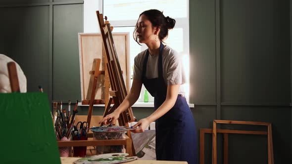 Art Studio  Young Woman Puts a Canvas on an Easel and Starts Painting