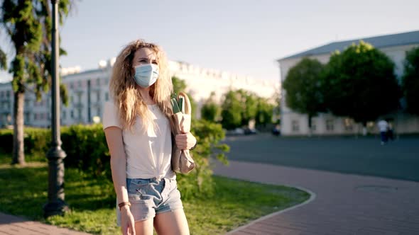 Caucasian Young Pretty Woman Delivery Worker in Medical Mask Walking the Street and Carrying Packet