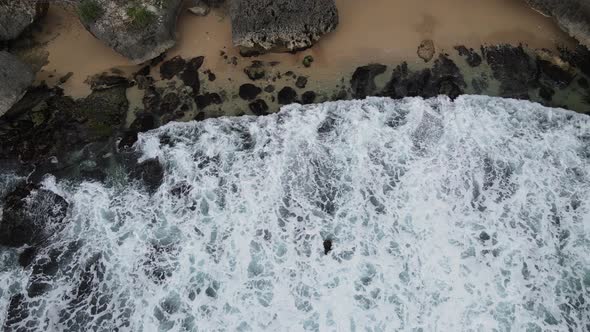 Top down aerial view of giant ocean waves crashing and foaming in coral beach