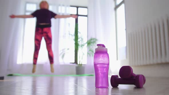 Fitness Training Overweight Woman Jumping on the Spot Bottle and Little Dumbbells on the Foreground