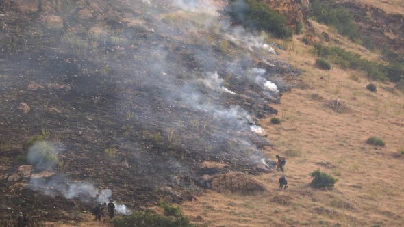 Firefighters working on wildfire as it burns on grass mountainside