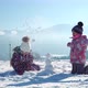Children in Outwear Making Small Snowman While Playing on Snowy Field in Sunlight with Mountains on - VideoHive Item for Sale
