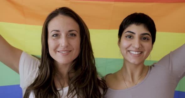 Happy girl friends lesbian couple holding a pride rainbow flag on background