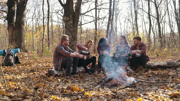 Group of tourists drinking hot tea near campfire in forest