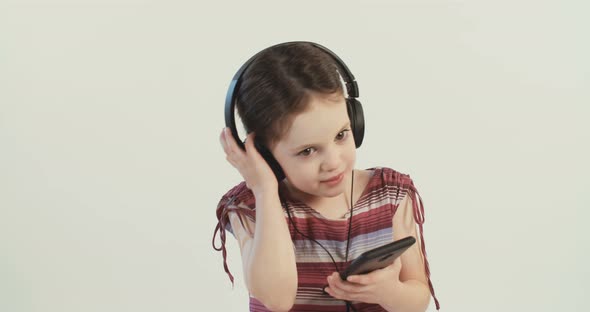 Little girl wearing a dress listening to music with earphones on a white studio background