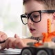 Smart boy in glasses programs a robot car and typing at a laptop at home. - VideoHive Item for Sale