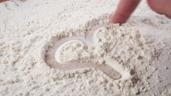 Chef draws a heart shape with his finger on a pile of flour