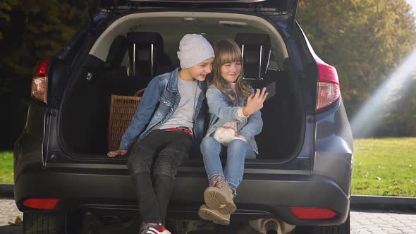 Attractive Portrait of Beautiful Happy Teen Children Which Sitting in the Trunk and Making Selfie