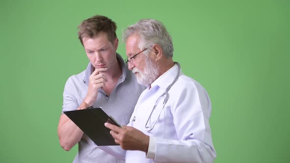 Senior Bearded Man Doctor Consulting Man Patient Against Green Background