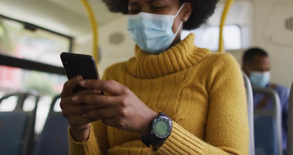 African american businesswoman with face mask using smartphone and sitting in bus