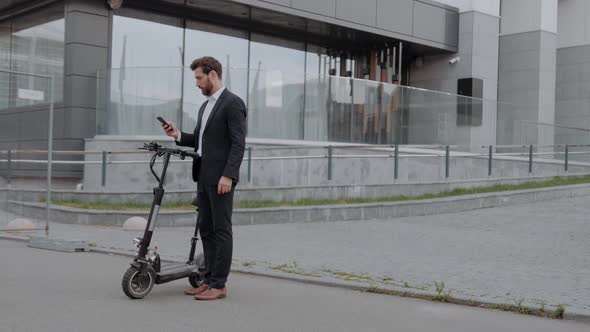 Businessman in a Suit is Activating an Electric Scooter with a Smartphone